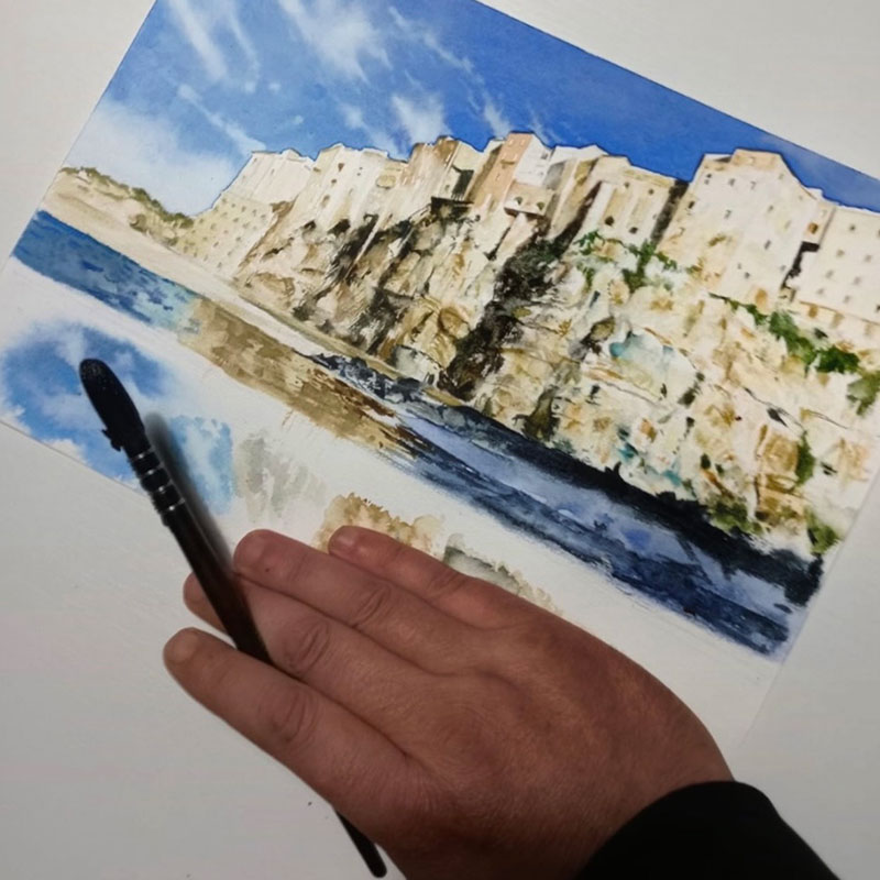Watercolour painting of Tropea cliffside, Calabria, southern Italy, with
artist's hand holding paintbrush