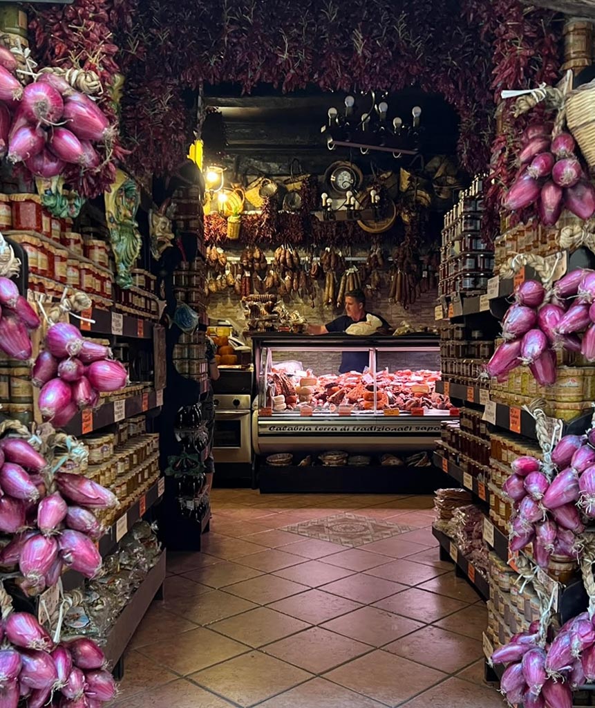 Artisan salumi shopfront in Tropea with hanging cured meats and red onions